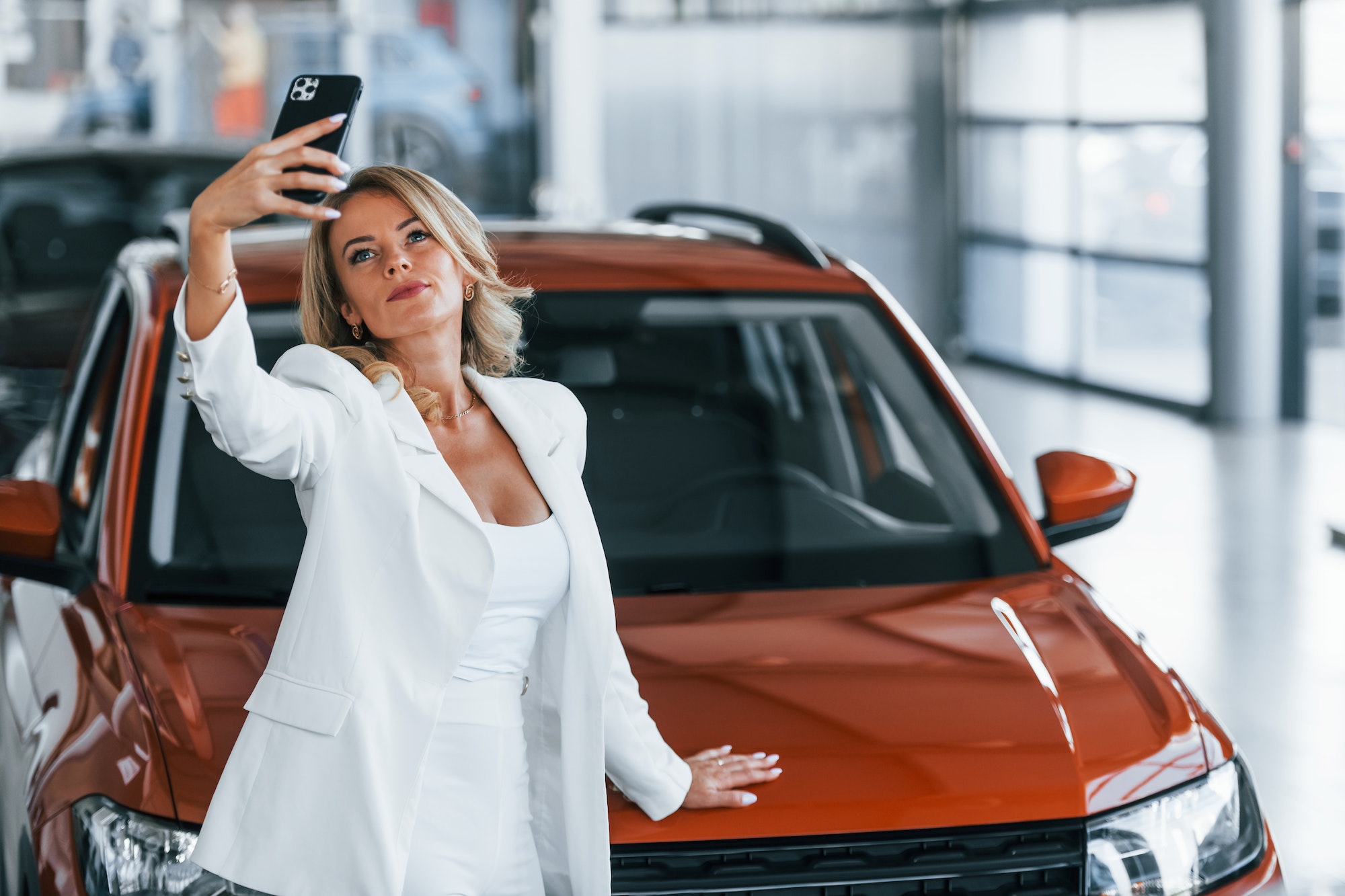 Making selfie. Woman in formal clothes is indoors in the autosalon